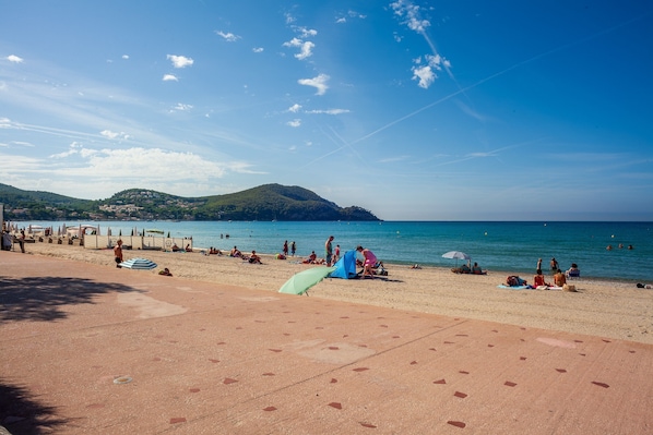 Una playa con gente tomando el sol y nadando, cielo despejado y una colina distante.
