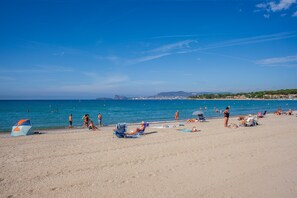 A beach with people sunbathing and swimming, a clear sky, and distant mountains.