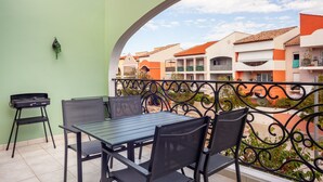 Un balcón con una mesa y sillas, una planta colgante y vistas de edificios cercanos.
