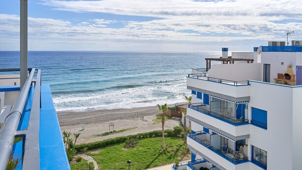 Ein Hotel an der Küste mit Balkonen, die auf den Strand blicken, bewölktem Himmel und Meerblick.