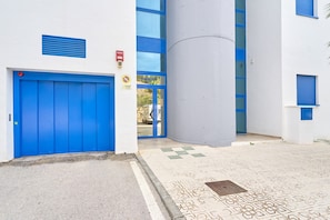 Een gevel met een blauwe deur, een brandmelder en een grote cilindervormige constructie.
