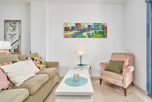 Een woonkamer met een bank, fauteuil, salontafel, lamp en een schilderij aan de muur.