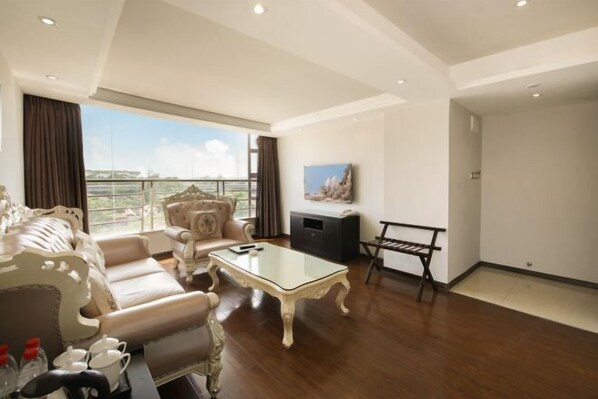 A spacious living room with a high ceiling, a large window offering a city view, a sofa set, a glass coffee table, and a small TV on the wall. - Mingji Hotel (Nansha Hotel, Guangzhou) (Guangzhou)