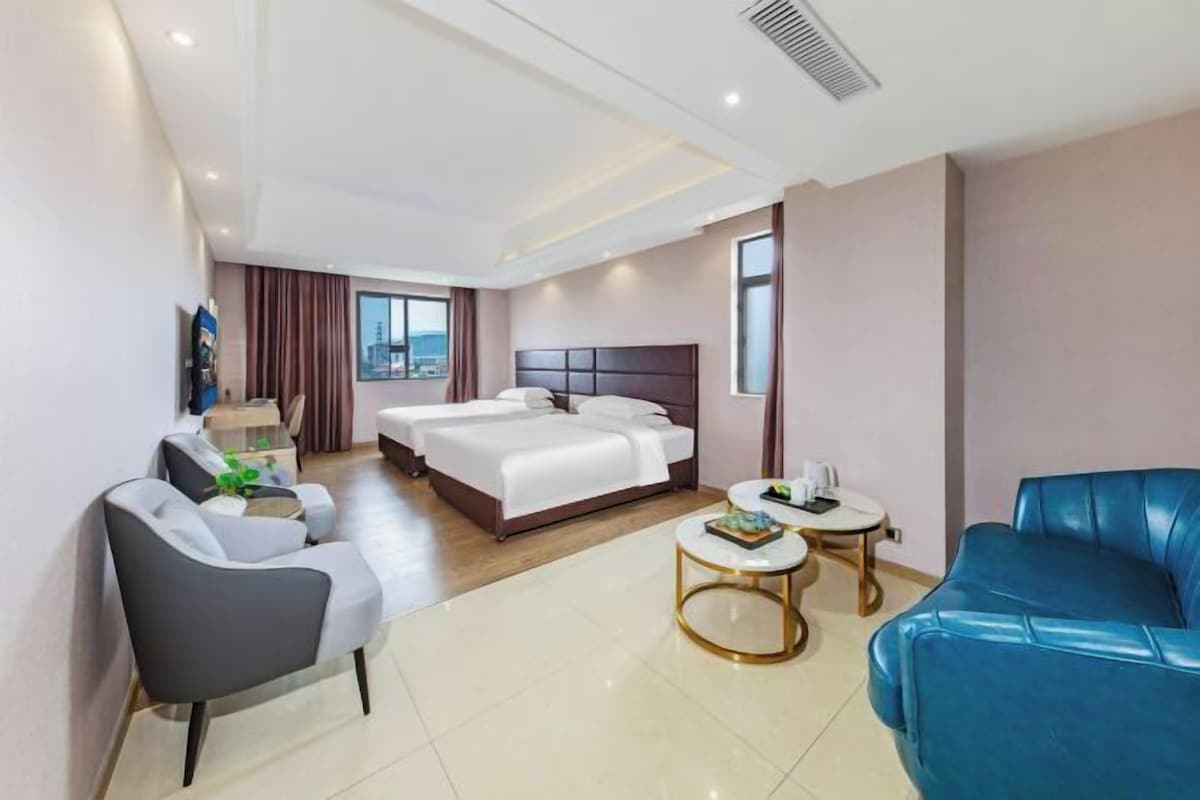 A hotel room with a bed, two bedside tables, a sofa, a chair, and a small table with a plant.