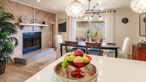 A modern dining area with a wooden wall, a fireplace, and a fruit bowl on the table. - HAPPY FUN  BLUE HOUSE for 8 people kids, pets friendly, 3 miles from the  beach🏖️ (Venice)