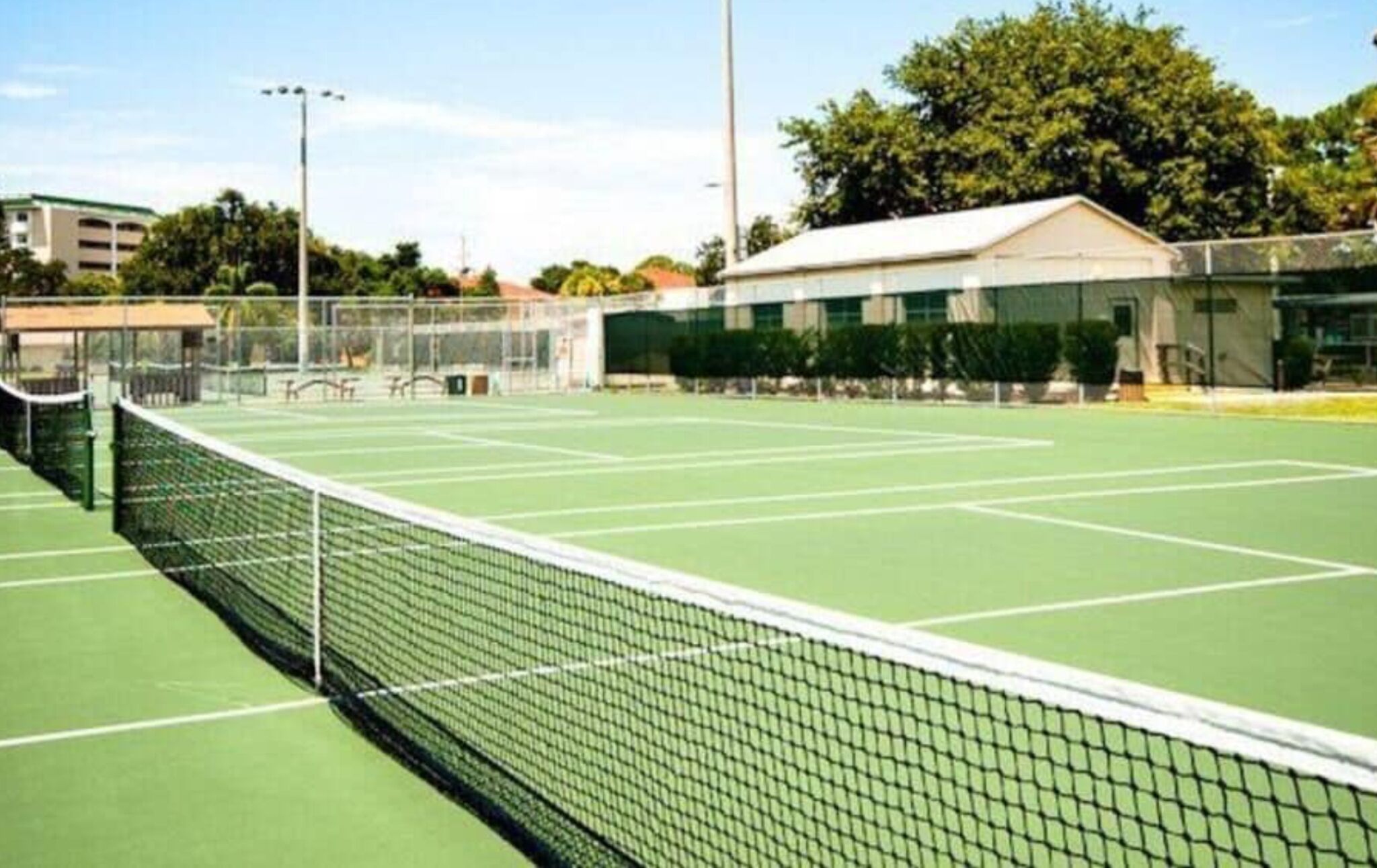 A tennis court with a net, surrounded by trees and buildings.