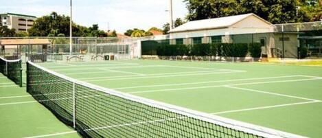 A tennis court with a net, surrounded by trees and buildings.