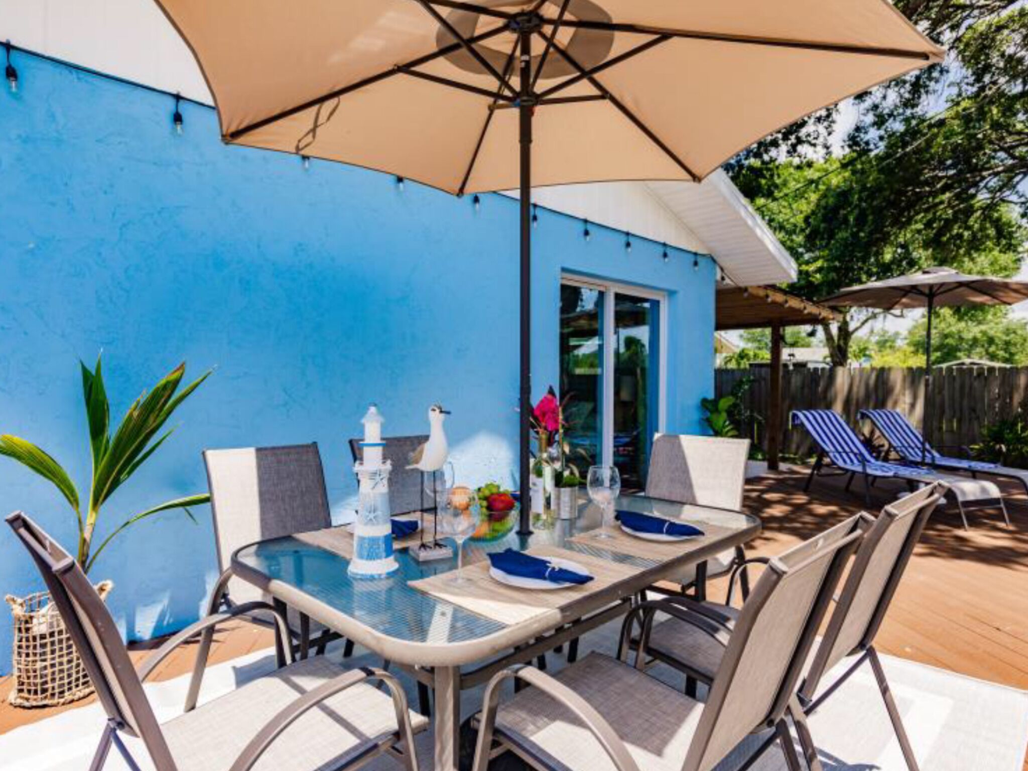 An outdoor patio with a table set for dining, surrounded by chairs, and shaded by a large umbrella.
