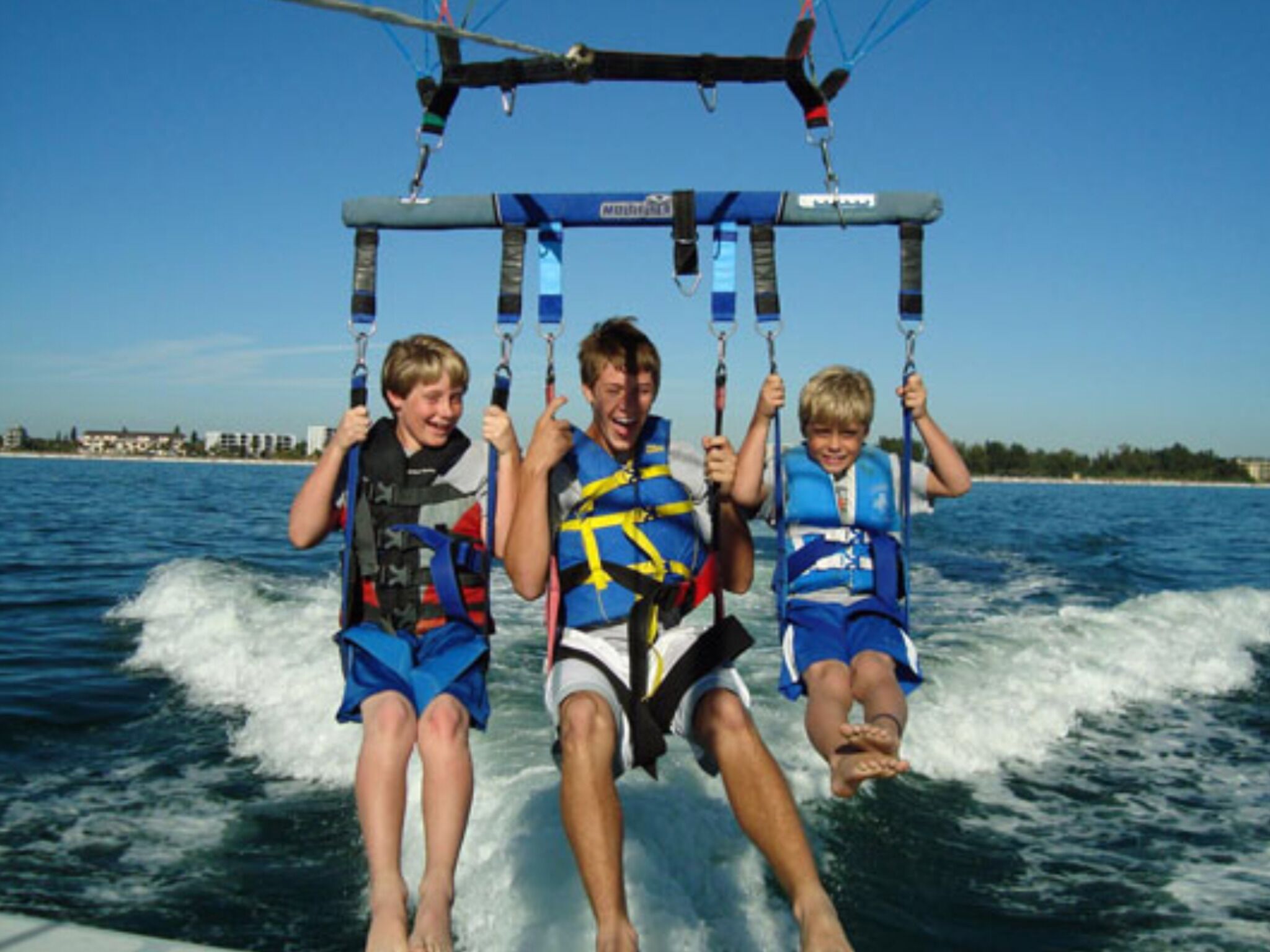 Drie personen beoefenen een watersport bij heldere hemel en rustig water.