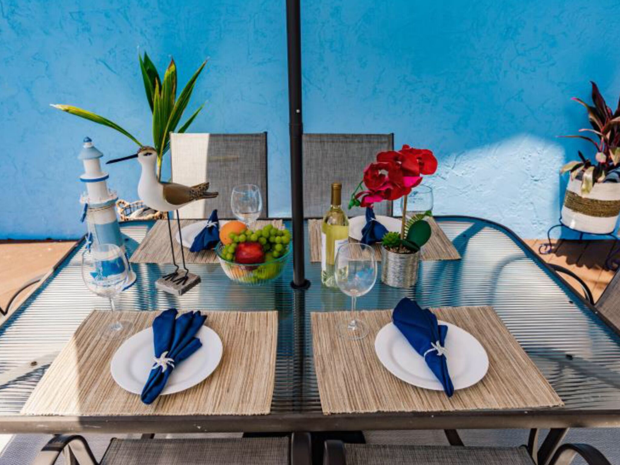 Una mesa de comedor con dos platos, una copa de vino, una botella de vino, un cuenco de fruta y un pájaro decorativo.