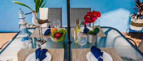 Una mesa de comedor con dos platos, una copa de vino, una botella de vino, un cuenco de fruta y un pájaro decorativo.