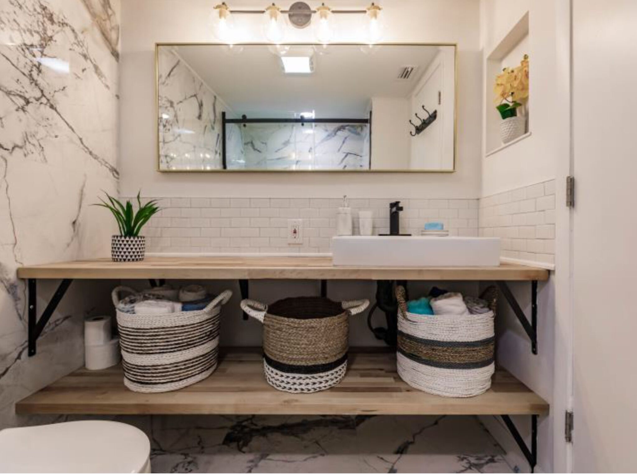 A bathroom with a marble wall, a sink, a mirror, and two baskets on a shelf.
