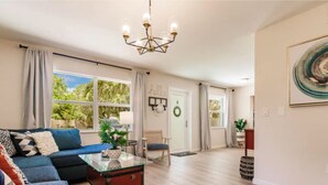 A spacious living room with a blue sofa, a glass coffee table, and a chandelier. - HAPPY FUN  BLUE HOUSE for 8 people kids, pets friendly, 3 miles from the  beach🏖️ (Venice)