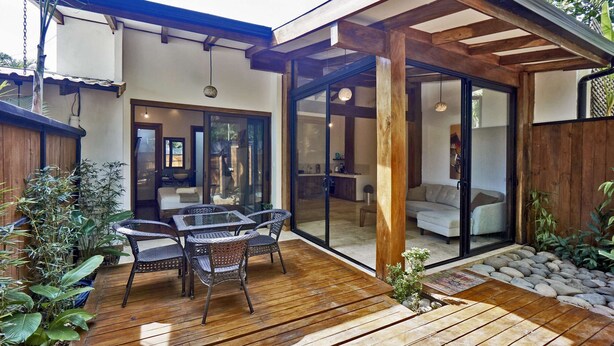 Une terrasse en bois avec des meubles d’extérieur, une porte vitrée donnant sur un espace de vie et une pergola en bois.
