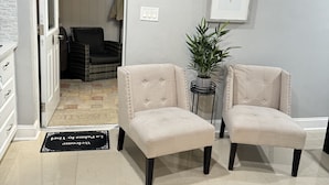 Une pièce avec deux fauteuils beiges, une plante en pot, un tableau encadré et une porte donnant sur un placard.
