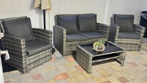 Un espace extérieur aménagé en terrasse, avec des meubles en osier, notamment un canapé et des fauteuils, ainsi qu’une table basse.