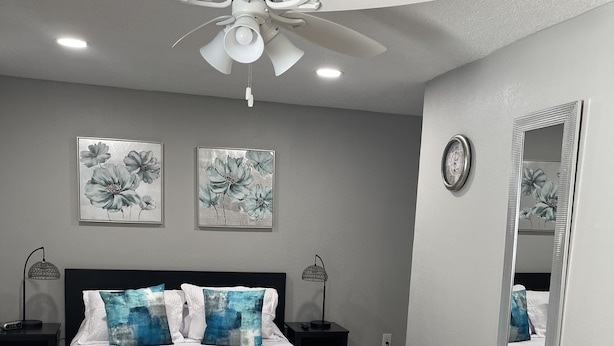 Une chambre à coucher comprenant un lit, un ventilateur de plafond, deux horloges murales et un miroir.