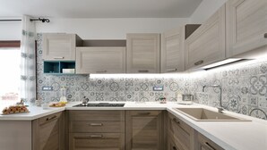 A modern kitchen with wooden cabinets, a white countertop, and patterned backsplash tiles. - Holiday Apartment 'Dolcecasa' with Mountain View, Private Terrace & Wi-Fi (Dorgali)
