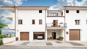 A two-story residential building with a garage, a balcony with potted plants, and a clear sky. - Holiday Apartment 'Dolcecasa' with Mountain View, Private Terrace & Wi-Fi (Dorgali)