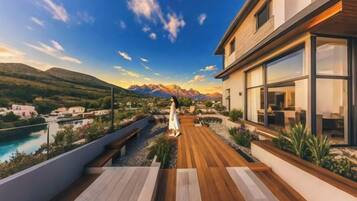 A modern building with a wooden deck, a pool, and mountains in the background.