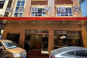 A hotel with a red awning and a sign in a foreign language. There are two cars parked in front. - Guoguang Hotel (Yizhang)
