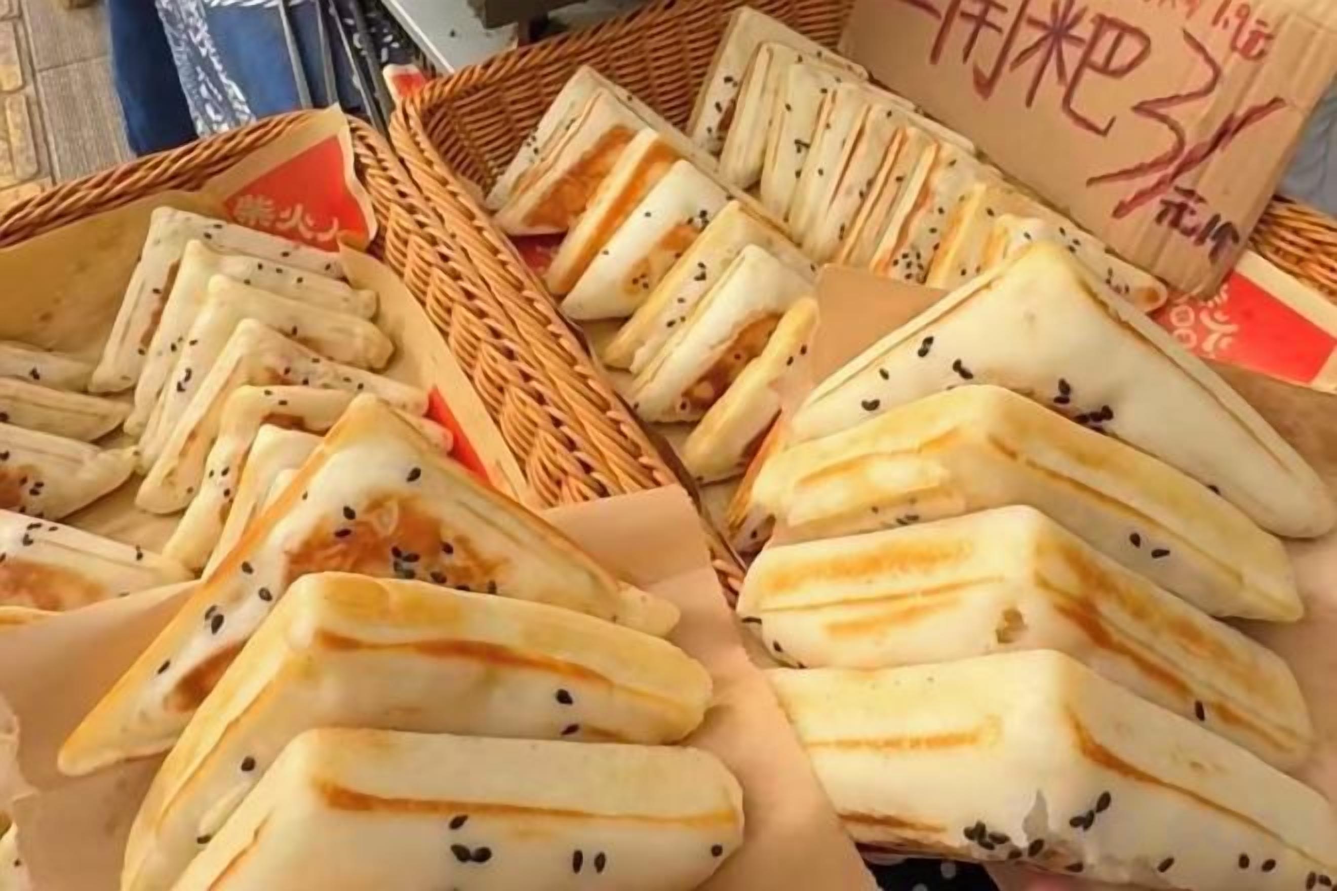 A display of triangular-shaped pastries with sesame seeds, arranged in baskets.
