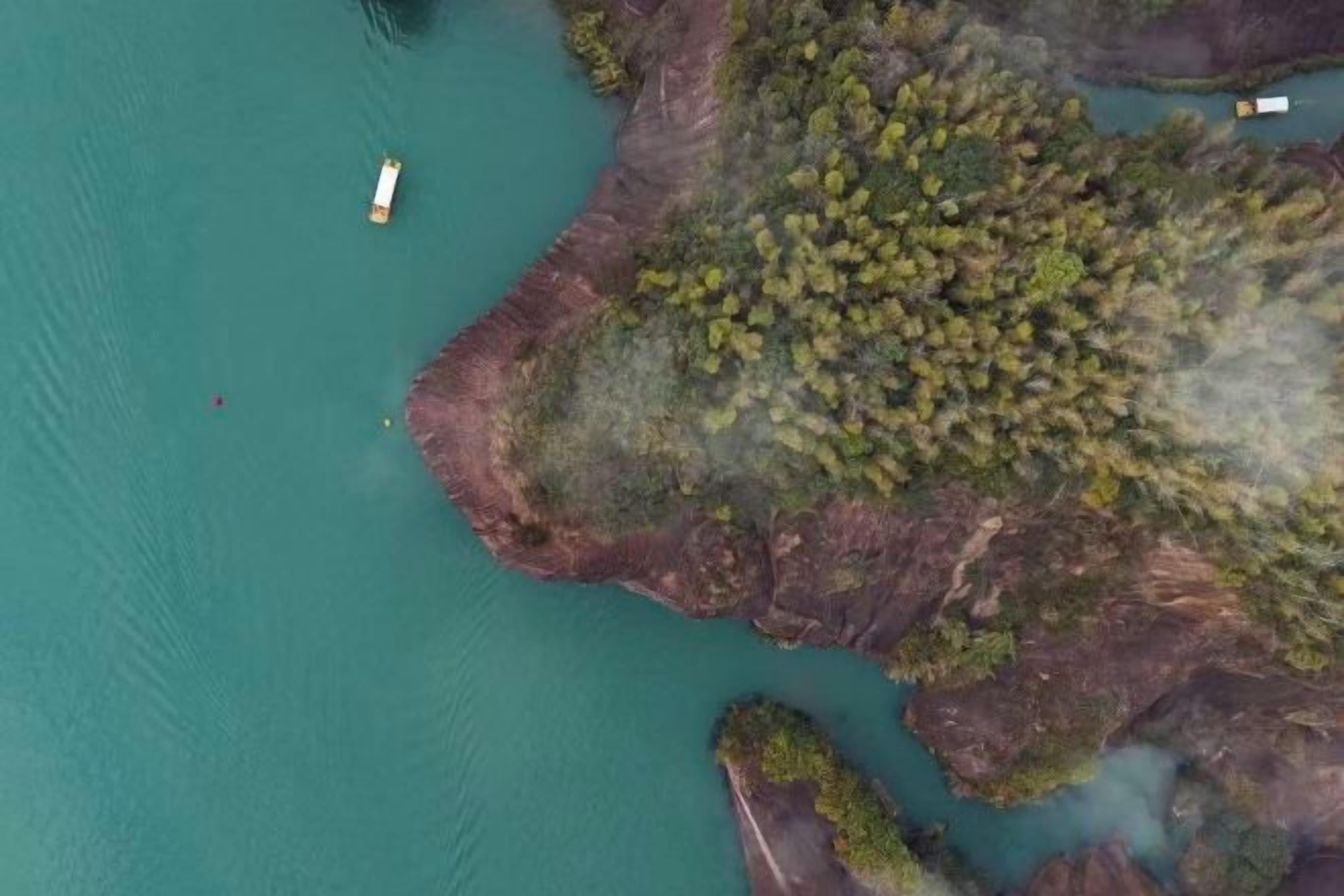 An aerial view of a coastal area with a boat, rocky terrain, and dense vegetation.