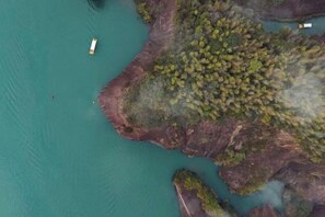 An aerial view of a coastal area with a boat, rocky terrain, and dense vegetation. - Guoguang Hotel (Yizhang)