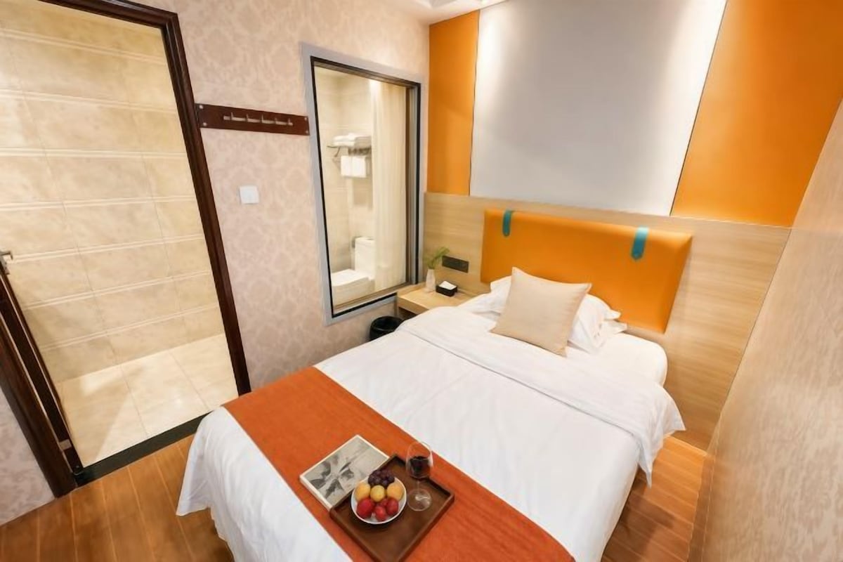 Habitación de hotel con cama, mesita de noche, espejo y puerta de baño.