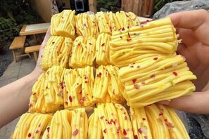 A person holding a tray of yellow, cylindrical food items with red specks, possibly a dessert or snack. - Guoguang Hotel (Yizhang)