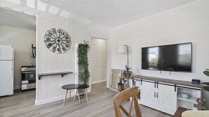 Et moderne køkken med indbygget ovn, spiseplads med et rundt bord og stole, et stort vægur og et fladskærms-tv på væggen.