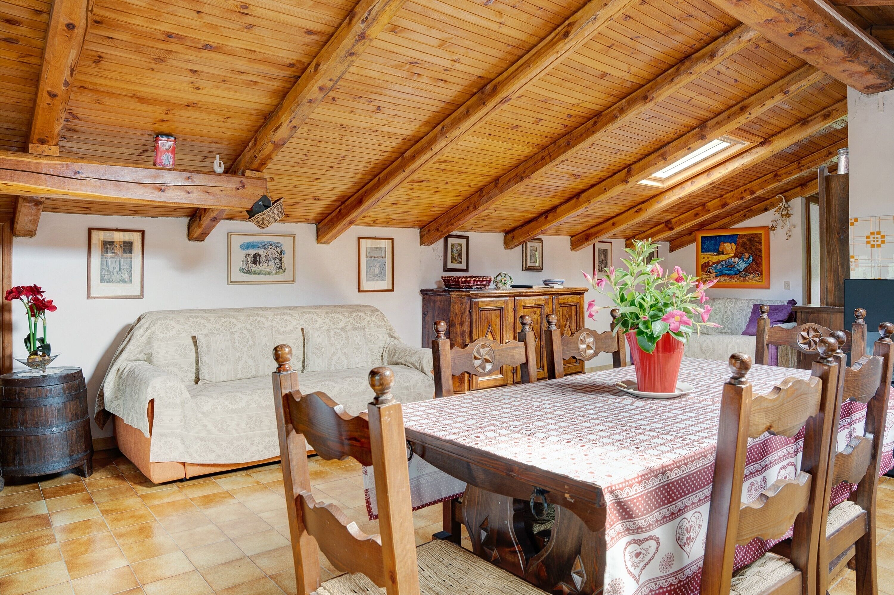 Una stanza accogliente con soffitto in legno, un divano, un tavolo da pranzo con sedie e una pianta in vaso.