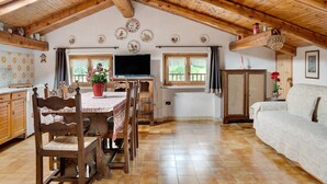Ein rustikaler Innenraum mit Holzbalkendecke, einem Esstisch mit Stühlen, einer Couch und einem Fernseher.