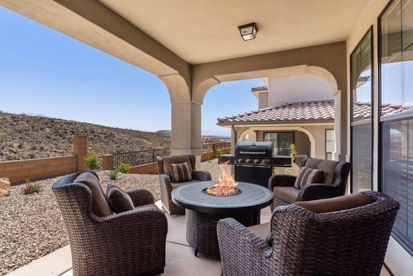 A covered patio with wicker furniture, a fire pit, and a grill.