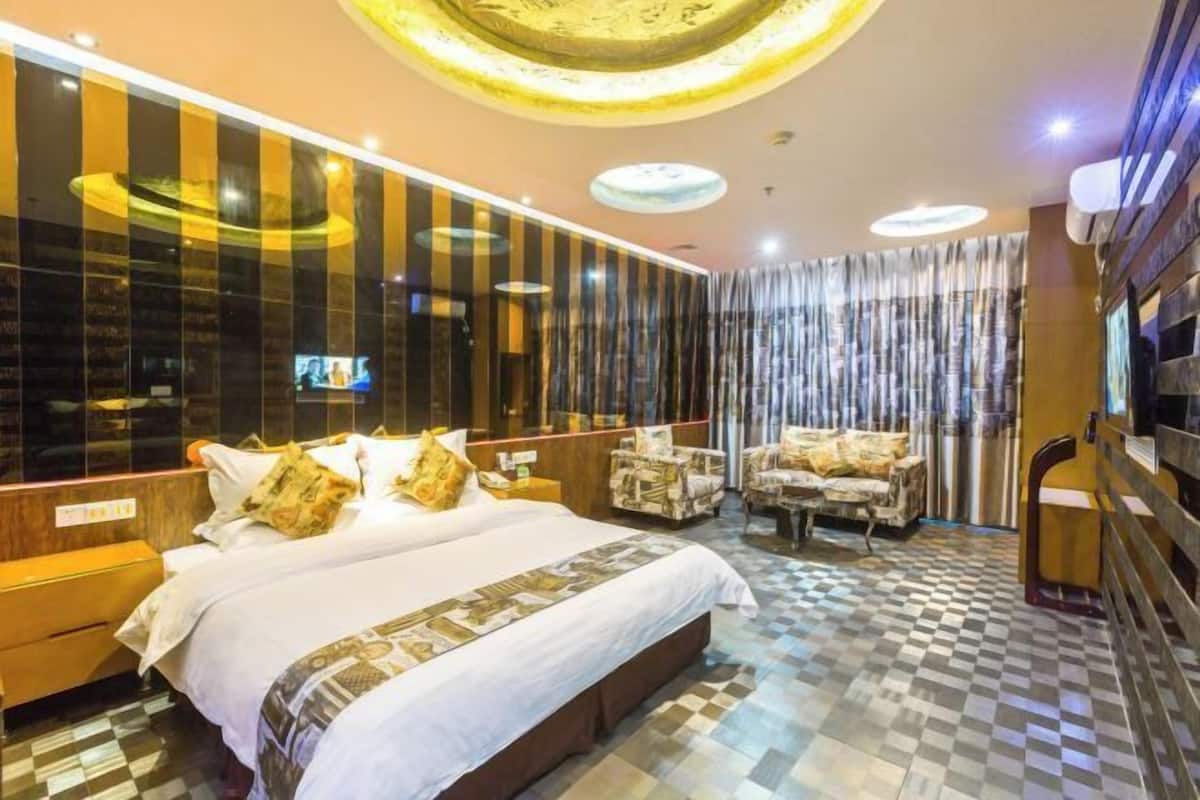 A hotel room with a large bed, a TV, a seating area with chairs, and a check-in counter.