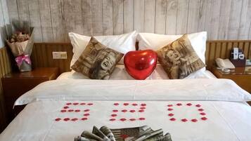 A bed with a heart-shaped pillow, a bouquet of flowers, and a red heart on the bedspread.