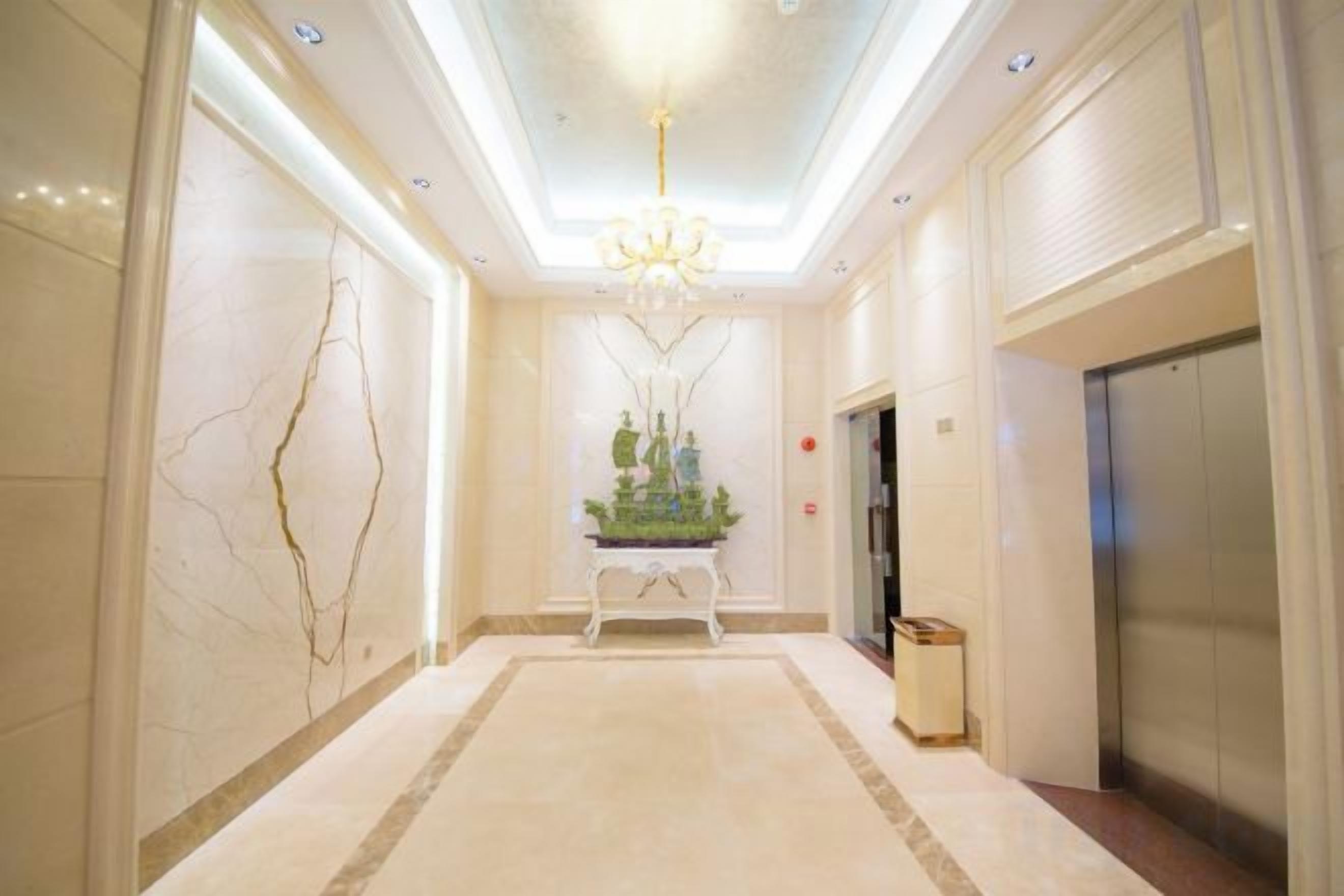 A hotel corridor with a marble floor, a chandelier, an elevator, and a trash bin.