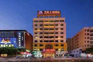 A multi-story hotel with a prominent sign at the top, multiple balconies, and a well-lit facade. - Mingxing Theme Hotel (Railway Station) (Heyuan)