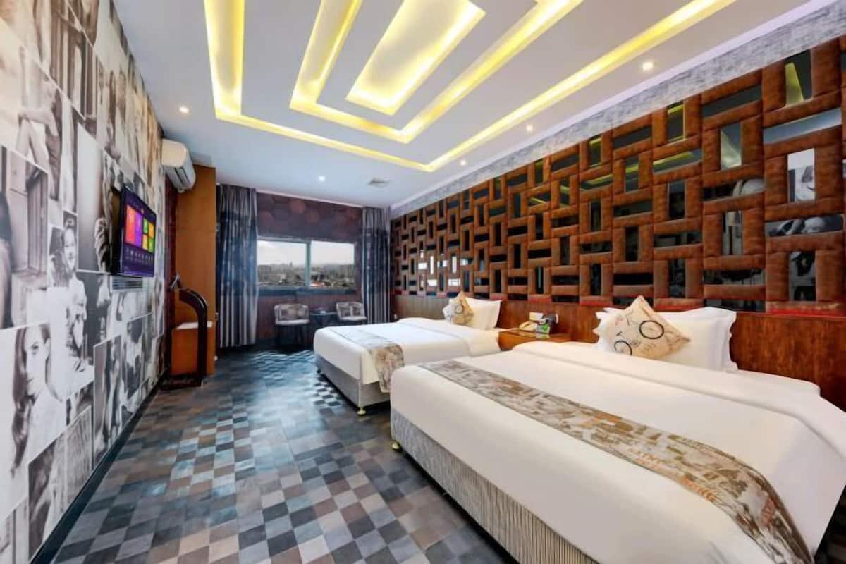 A hotel room with two beds, a patterned floor, a wall with a geometric design, and a city view through the window.