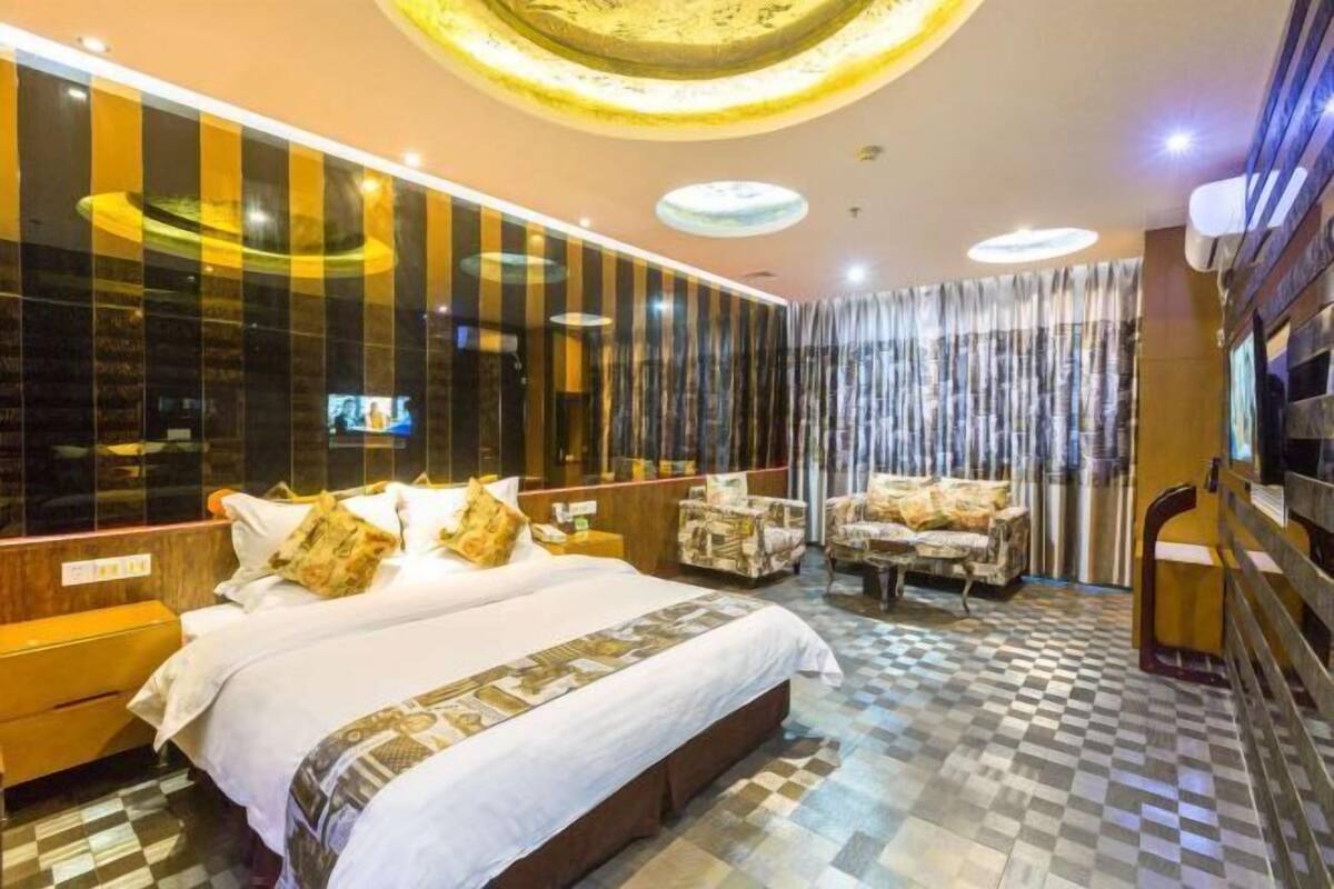 A hotel room with a large bed, a TV, a seating area with chairs, and a check-in counter.