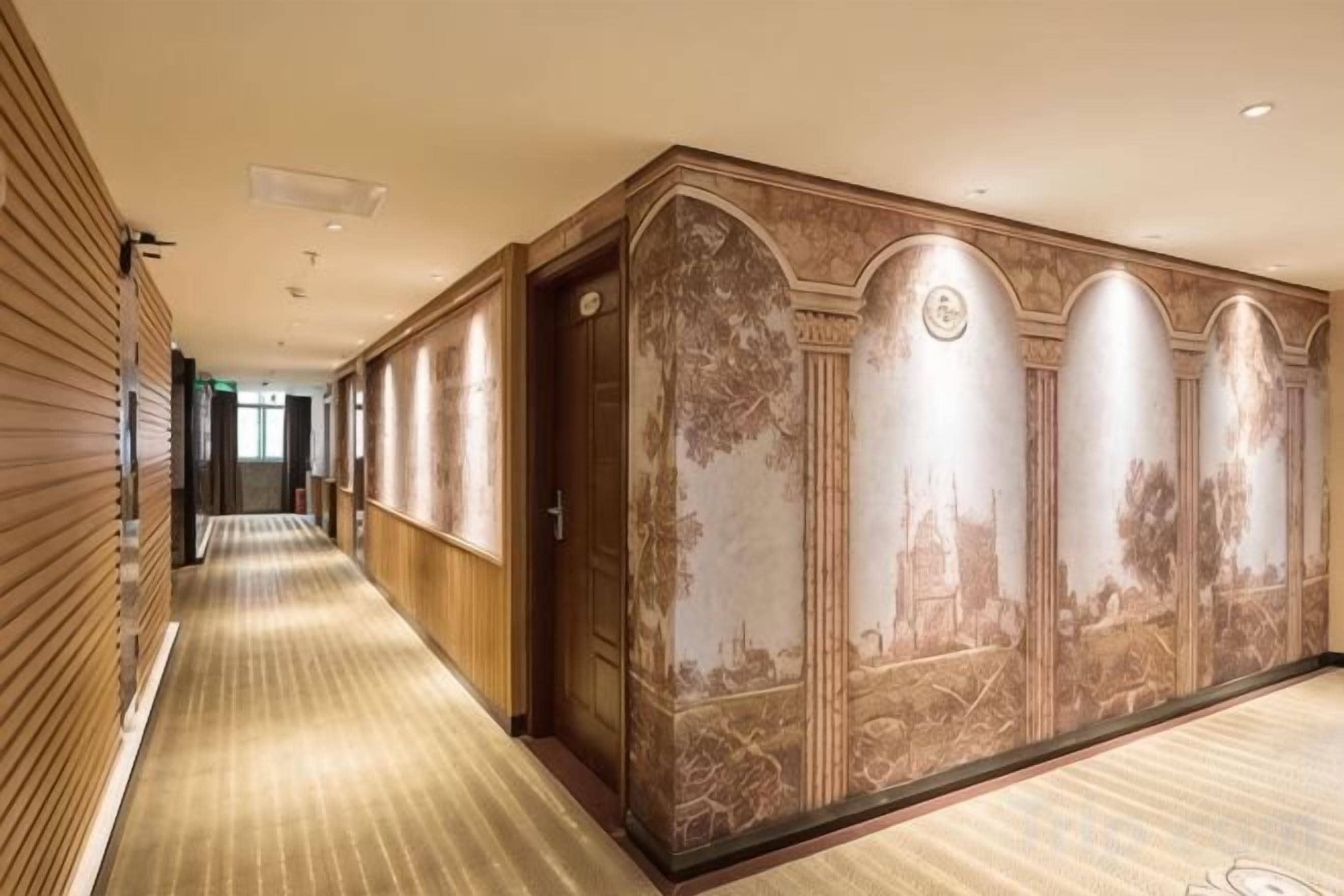 A hotel corridor with a patterned carpet, wooden paneling, and a mural with architectural elements.