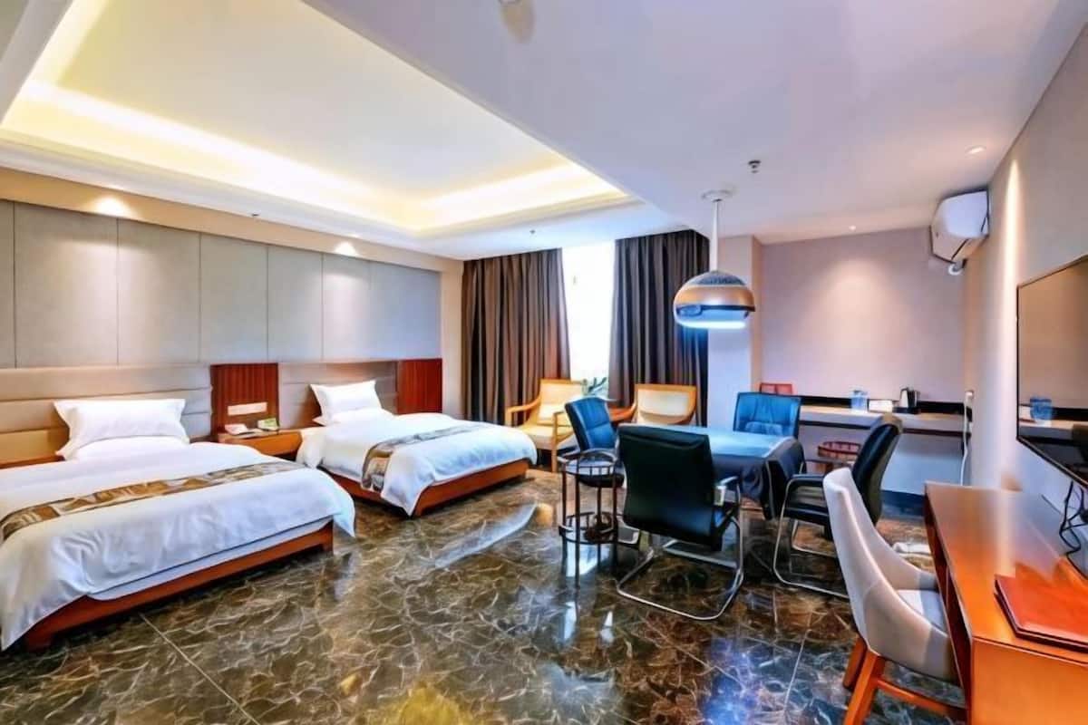 A hotel room with two beds, a desk, a chair, a lamp, and a television.