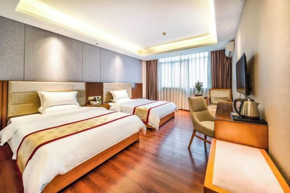A hotel room with two beds, a desk, a chair, a TV, and a window with curtains.