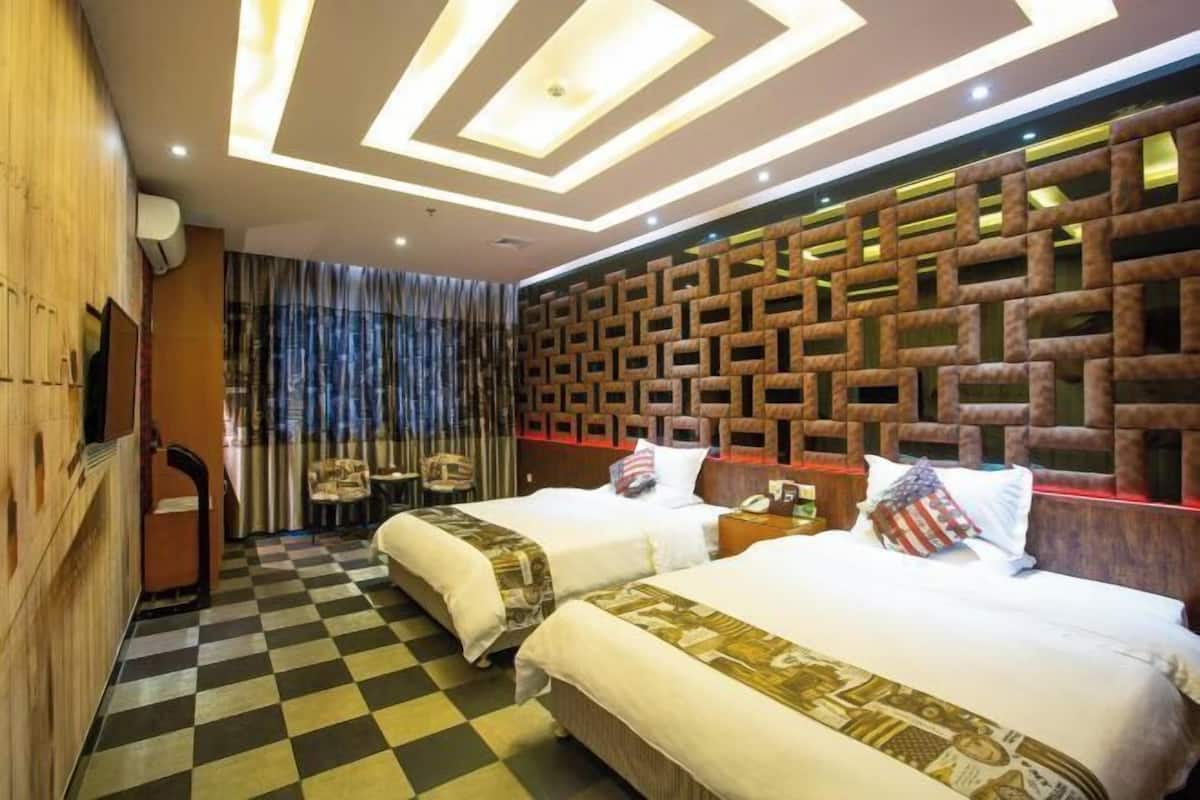 A hotel room with two beds, a checkered floor, a patterned headboard, and a wooden wardrobe.