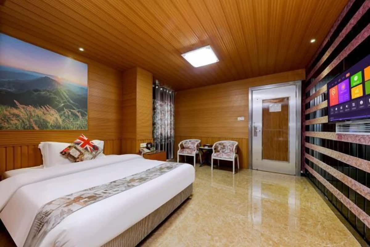 A hotel room with a large bed, a painting of a landscape, a flat-screen TV, and a wooden ceiling.
