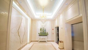 Um hall de hotel moderno com piso de mármore, um arranjo de plantas decorativo e um elevador.