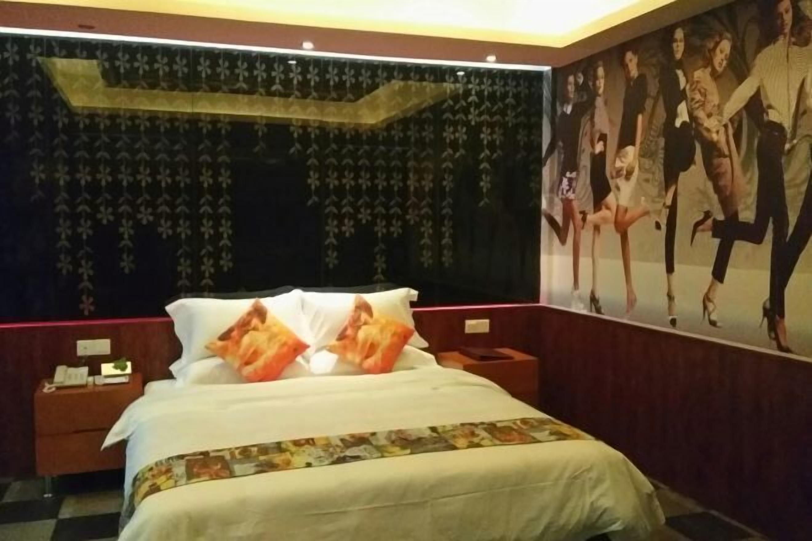 Habitación de hotel con una cama grande, una mesita de noche, un televisor montado en la pared y un cartel de bailarines.