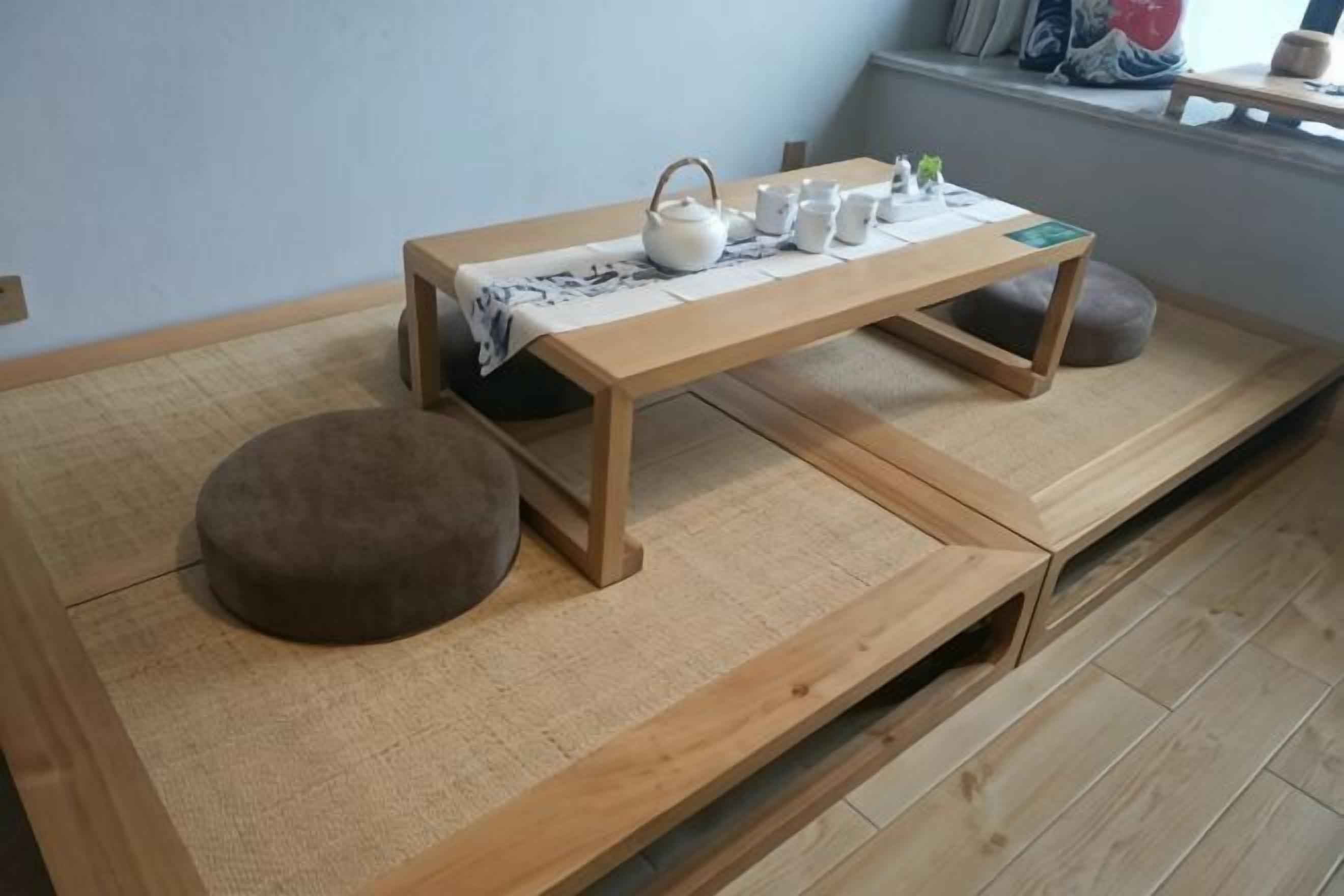 A room with tatami flooring, a wooden table with a tea set, and a cushion.