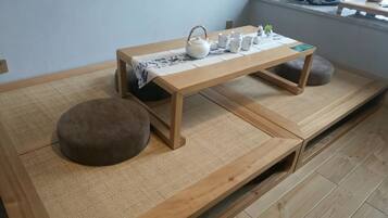 A room with tatami flooring, a wooden table with a tea set, and a cushion.