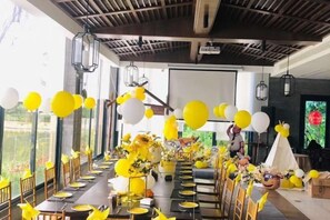 A long dining table set for a celebration with yellow and white balloons, floral centerpieces, and a projector screen in the background. - Aile Holiday Hotel (Sanming)